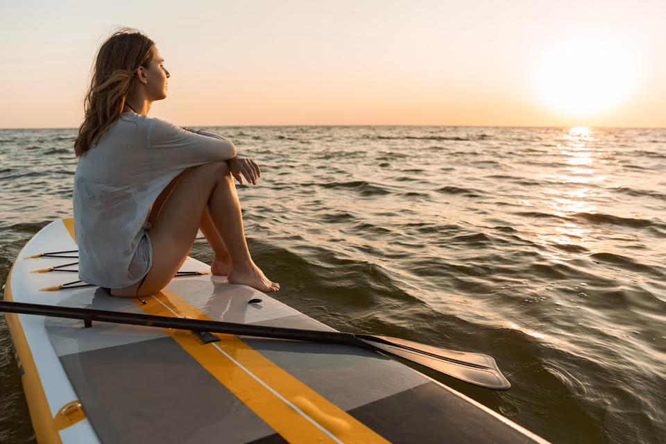 Frau sitzt bei Sonnenuntergang auf einem Stand-up-Paddleboard am Wasser