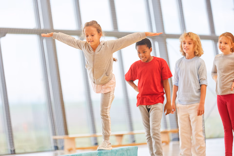 Kinder balancieren in einer Turnhalle über einen Balken